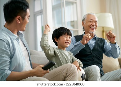 asian son father grandfather sitting on couch at home celebrating goal and victory while watching live broadcasting of football match on TV together - Powered by Shutterstock