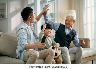 asian son father grandfather sitting on couch at home celebrating goal and victory while watching live broadcasting of football match on TV together - Powered by Shutterstock