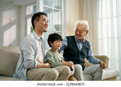 asian son father grandfather sitting on couch at home celebrating goal and victory while watching live broadcasting of football match on TV together - Powered by Shutterstock