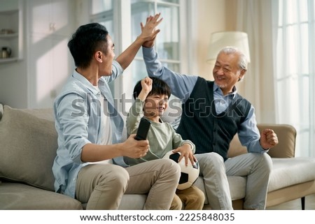 asian son father grandfather sitting on couch at home celebrating goal and victory while watching live broadcasting of football match on TV together Stock photo © 