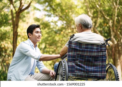 asian son talking to and comforting wheelchair bound father