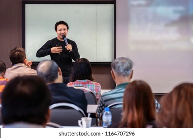 Asian Speaker or lecture with casual suit on the stage in front of the room presenting with the screen in the conference hall or seminar meeting room, business and education concept