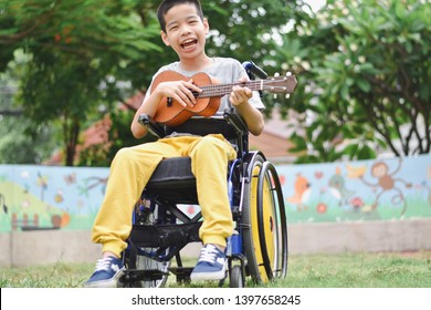 Asian special child on wheelchair is playing ukulele happily on the playground, nature background, Life in the education age of disabled children, Happy disabled kid concept.