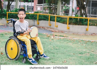 Asian Special Child On Wheelchair Is Playing Musical Equipment Happily On The Playground, Nature Background And Sun Light, Life In The Education Age Of Disabled Children, Happy Disability Kid Concept.