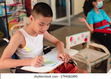 Asian Special Child On Wheelchair And Wood Trays For Activities With Smile Happy Face While Doing Art At Classroom In School,Life In The Education Age Of Disabled Children, Happy Disabled Kid Concept.