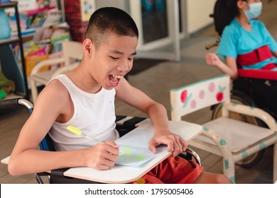 Asian Special Child On Wheelchair And Wood Trays For Activities With Smile Happy Face While Doing Art At Classroom In School,Life In The Education Age Of Disabled Children, Happy Disabled Kid Concept.