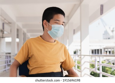 Asian Special Child On Wheelchair Wearing A Protection Mask Against PM 2.5 Air Pollution And Flu Covid 19 Or Coronavirus On Public Path Background, N95 To Prevent The Spread Of The Virus Disease 2021.