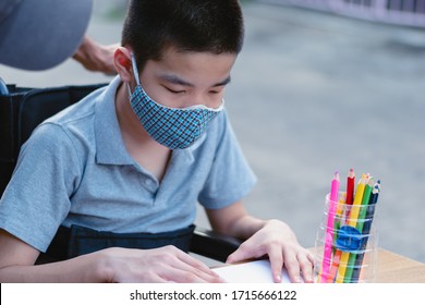 Asian Special Need Child On Wheelchair Wearing A Cotton Mask By Parent, The Boy Doing Home Work, Study And Working At Home For Safety From Covid 19, Life In Education Age Of Disabled Children.