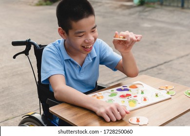 Asian Special Need Child On Wheelchair Interested In Skills Development Toy On Home Nature Background,Education For Disabled Children Style,Boy Plays Fruit Jigsaw Puzzles,Happy Disability Kid Concept.