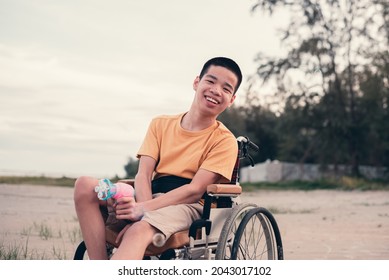 Asian special teenager boy on wheelchair is smiling happiness face holding bubble gun toy on nature outdoor, Happy disabled kid travel and mental healthy concept.