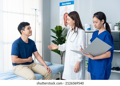 Asian Specialist Doctor And Assistant Nurse Take Care Of Male Patient. Professional Female Physician Team Explain Diagnosis And Advise Service Treatment To Sick Person In Hospital During Appointment.