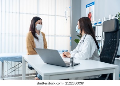 Asian Specialist Woman Doctor Explain Diagnosis To Young Girl Patient. Professional Female Physician Wear Mask Due To Covid And Advise Treatment Plan To Sick Person In Hospital During The Appointment.