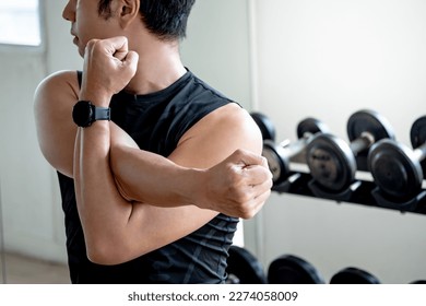 Asian sport man in black sportswear stretching arms with cross-body shoulder stretch pose and warming up before weight training in fitness gym. Physical exercise posture for muscle stretching.