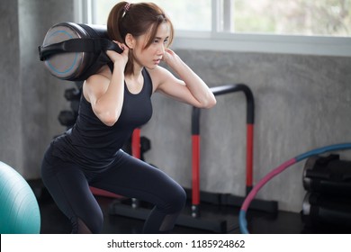 Asian Sport Woman In Sportswear Exercise Squat With With Training Weight Bag In Fitness Gym . Young Girl Workout With Lifting Weights Bags. Building Muscles  Bodybuilding.