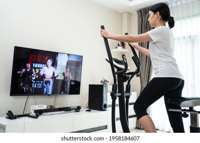 Asian Sport Woman Workout Exercising By Watching Fitness Live Or Video Tutorial TV Online On Television At Home. Casual Young Girl Using Exercise Bike Follow Instruction From Trainer During Quarantine