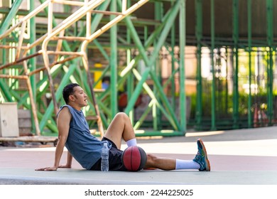 Asian sportsman basketball player resting on the floor and drinking water from a bottle after do sport training and playing streetball on outdoors court under highway in the city in summer sunny day. - Powered by Shutterstock