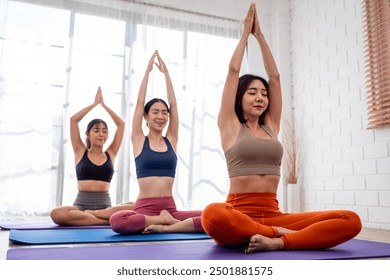 Asian sportswoman friends doing yoga pilates workout together at home. Attractive women trainer in sportswear leading practice stretching pose exercise to student during yoga class in fitness studio. - Powered by Shutterstock