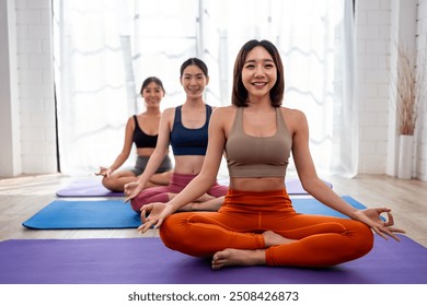 Asian sportswoman friends doing yoga pilates workout together at home. Attractive women trainer in sportswear leading practice stretching pose exercise to student during yoga class in fitness studio. - Powered by Shutterstock