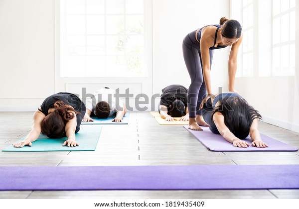 Asian sporty people learning Yoga class in\
fitness club. Instructor coaching and adjust correct pose on child\
pose to student. Yoga Practice Work out fitness healthy lifestyle\
concept.