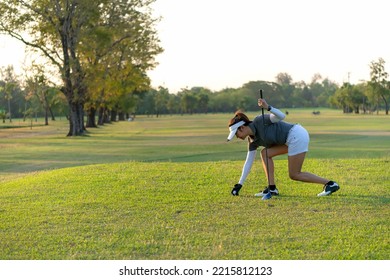 Asian Sporty Woman Putt Golf Ball On Tee Off With Club In Golf Course On Evening On Time For Healthy Sport Sunset Background. Lifestyle And Sport Concept