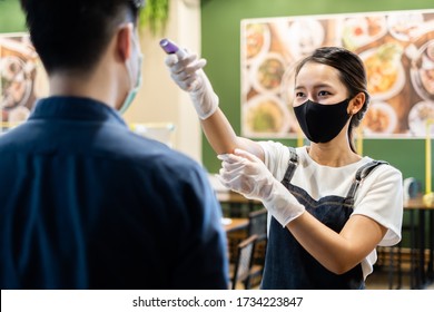 Asian Staff Restaurant Waitress Wear Protective Face Mask Scan Customer Temperature By Thermometer Before Entering The Restaurant To Protect Infection From Flu Fever And Coronavirus Covid-19