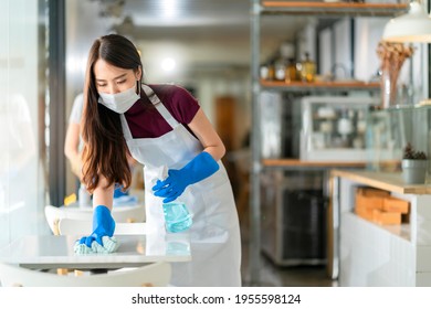 asian staff waitress wearing protection face mask apron and rubber glove cleaning table with disinfectant alcohol spray for prevent infection coronavirus in cafe coffee shop new normal concept - Powered by Shutterstock