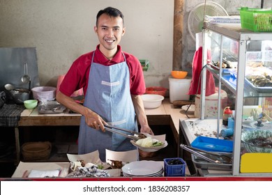 Asian stall waiters stand holding tongs while preparing side dishes for customers' orders at the stall