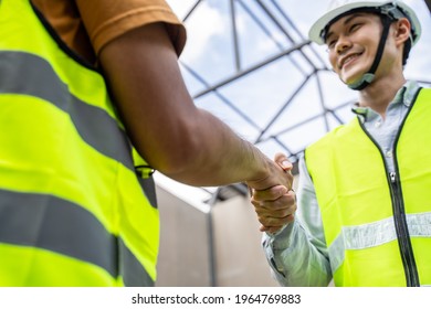 Asian Structure Engineer And Worker Making Handshake On Building Working Site. All People Wearing Safety Hardhat During Walking In Construction Workplace. Business Deal, Merger And Acquisition Concept