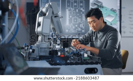 Asian Student Assembling Robotic Arm with Screwdriver During the Lesson. Robot is Moving. Computer Motherboard Components at Digital Interactive Whiteboard at Background. Education Concept