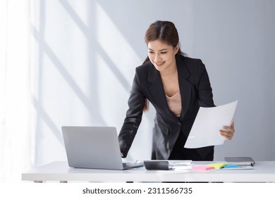 Asian student business woman using calculator and laptop for doing math finance on an office desk, tax, report, accounting, statistics, and analytical research concept