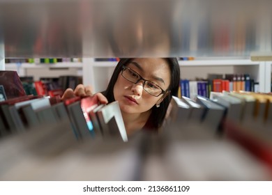 Asian Student Choosing Book In College Library. Young Girl Learning In University. Female In Eyeglasses Preparing For Literature Test Or Exam. Ethnic Teenager Study In High School. Education Concept