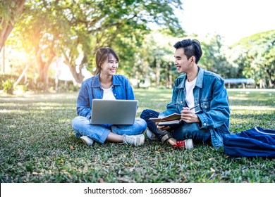 Asian Student Couple Studying Outside On The Grass, Sitting Down On The School Campus Using Laptop Computer, Books, Pencil And Note Book, Studying Hard Under The Trees Nature In The Evening Sunlight