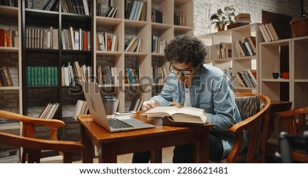 Asian student doing research in library using laptop in books, making a project and preparing for exam. Nerdy guy studying his lessons - education, self-study concept close up