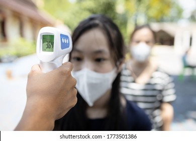 Asian student girl wear medical face mask is checking fever outside of school during its reopening after COVID-19 lockdown,screen people check body temperature with contactless thermometer,new normal - Powered by Shutterstock