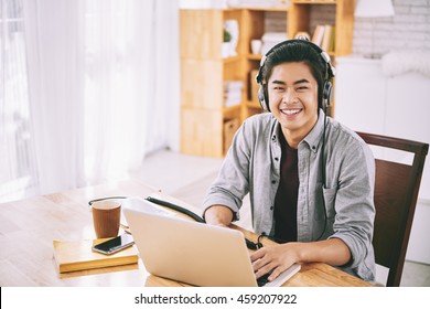 Asian student in headphones working on laptop at home