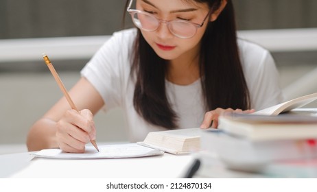 Asian Student Women Reading Books In Library At University. Young Undergraduate Girl Do Homework, Read Textbook, Study Hard For Knowledge And Education On Lecture Desk At College Campus.