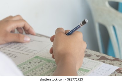 Asian Students holding pencil in hand doing multiple-choice quizzes or testing exams answer sheets exercises on old wood table In secondary school, college university classroom in education concept
