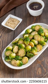 Asian style Brussels Sprout Salad. Sliced Brussels Sprouts Pickled in dashi soy sauce marinade sprinkled with sesame seeds on a white plate. Wooden table, selective focus, vertical. - Shutterstock ID 2250606115