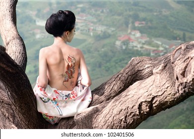 Asian Style Portrait Of Young Woman Sitting On The Tree Branch With Snake Tattoo On Her Back (original)