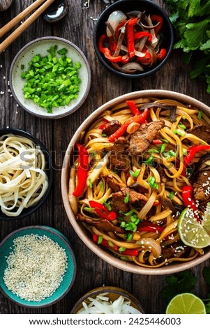 Asian style stir fried vegetables, roast beef and chow mein noodles to go in food box on wooden table 