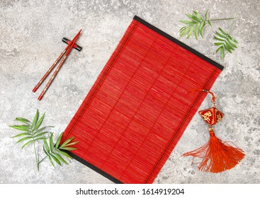 Asian Style Table Place Setting With Chinese New Year Ornament. Lucky Charm, Chopsticks, Red Bamboo Mat