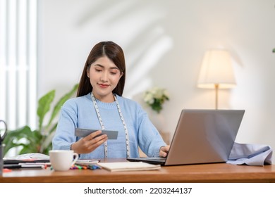 Asian Stylish And Designer Woman Working With Pantone Or Color Palettes For New Cloth Or Dressmaking Collection. Fashion Designer Tailor Looking In Color Sample To Selection In Her Workshop