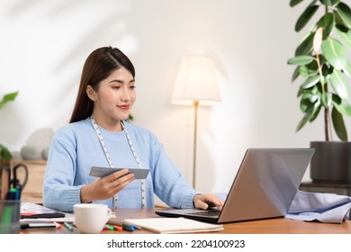 Asian Stylish And Designer Woman Working With Pantone Or Color Palettes For New Cloth Or Dressmaking Collection. Fashion Designer Tailor Looking In Color Sample To Selection In Her Workshop