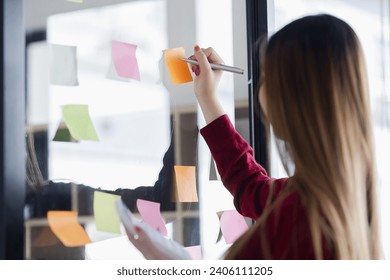 Asian successful businesswoman writing on paper note behind glass board in meeting room, Happy woman using colorful sticky paper on glass wall at office. - Powered by Shutterstock