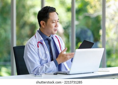 Asian Successful Professional Middle Aged Male Doctor In White Lab Coat With Stethoscope Sitting Using Laptop Notebook Computer Working Researching Online In Glass Windows Hospital Clinical Office.