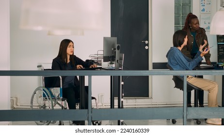 Asian system engineer with impairment programming app script on terminal window, using big data language. Developer in wheelchair working with cloud computing database, firewall security.