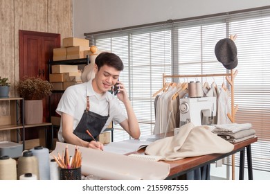 Asian tailor male talking on phone with customer and clothes sketch in tailoring atelier, start up young man fashion designer working and talking with client on smartphone. - Powered by Shutterstock