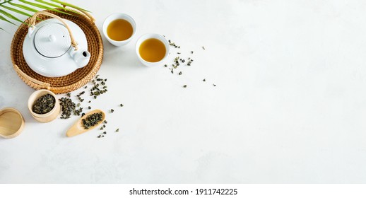 Asian tea concept, two white cups of tea and teapot surrounded with green dry tea  with space for a text on light background. Wide banner.