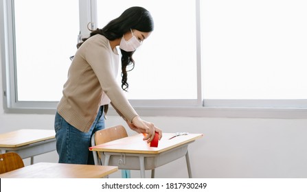 Asian Teacher In A Medical Mask Marking Places In The Classroom For Returning Of Students After Covid19 Quarantine And Lockdown. Social Distancing. Focus Hand.