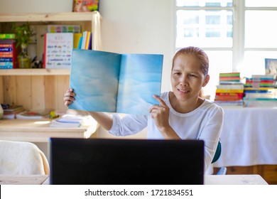 Asian Teacher Online Learning.Female Showing Story Book. Kindergarten And Preschool Reading Lesson Through Laptop Because Of Corona Virus Lockdown. Homeschooling Through Video Call.